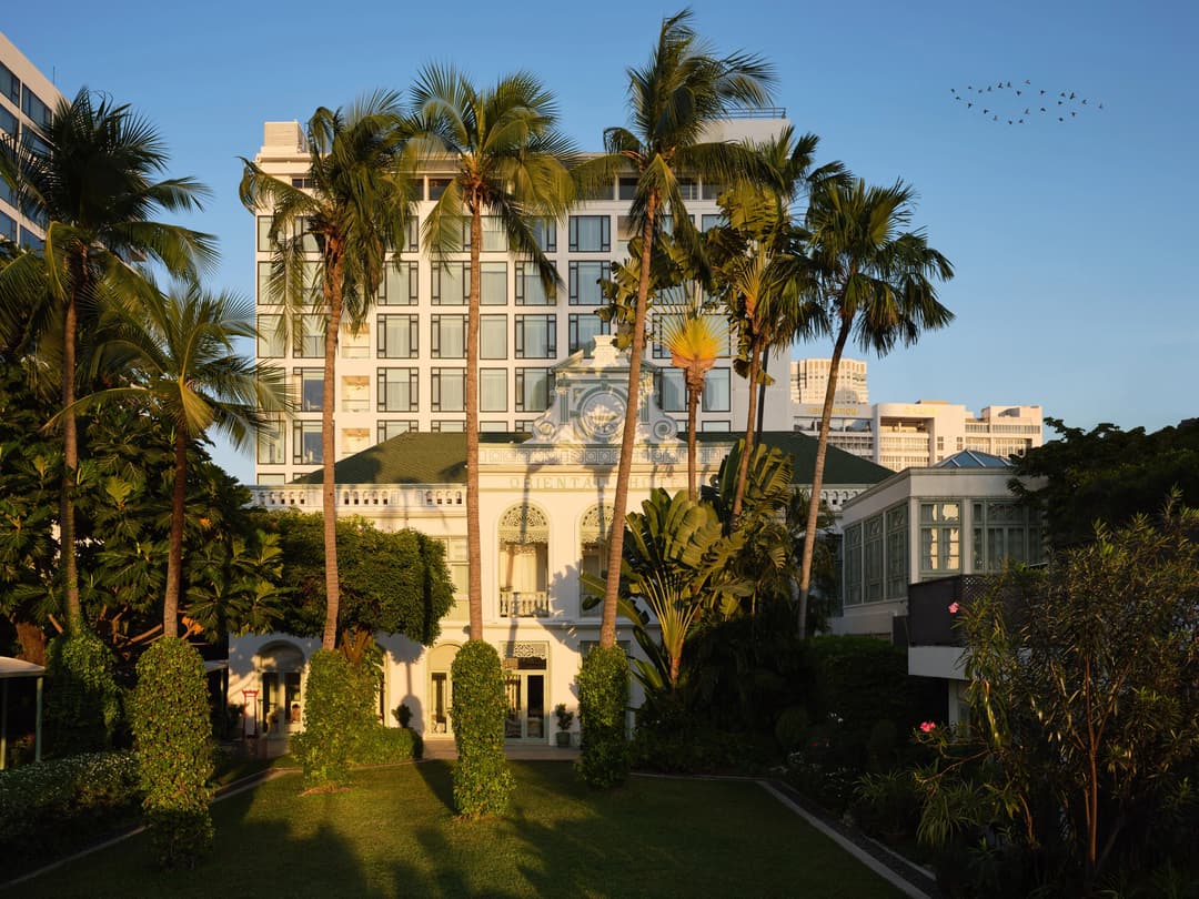 Mandarin Oriental, Bangkok exterior facade at sunset, surrounded by tall palm trees and historic architecture in warm golden light, Mandarin Oriental