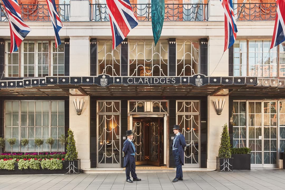 Claridge’s hotel entrance with Union Jack flags above the canopy and two uniformed doormen standing outside the doors, Claridge's