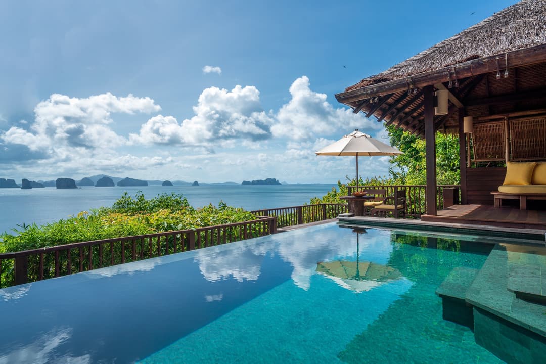 Serene pool next to a wooden villa, facing the ocean, with views of gentle waves, islands in the distance, and soft clouds overhead, Six Senses Yao No
