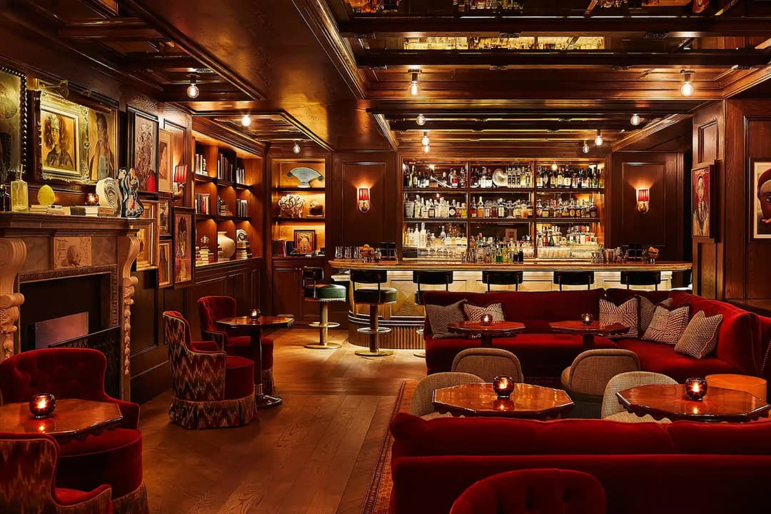 Bar with red velvet banquettes, a fireplace and framed paintings at The Fifth Avenue Hotel