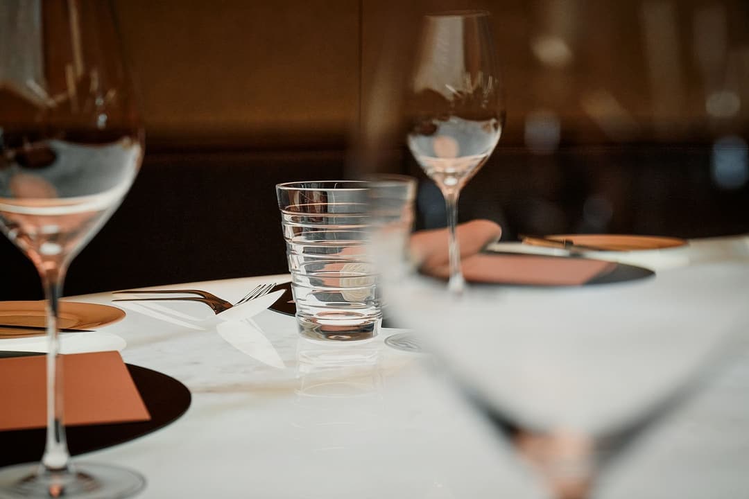 Table setting with wine and water glasses and folded orange napkins at The Dolder Grand