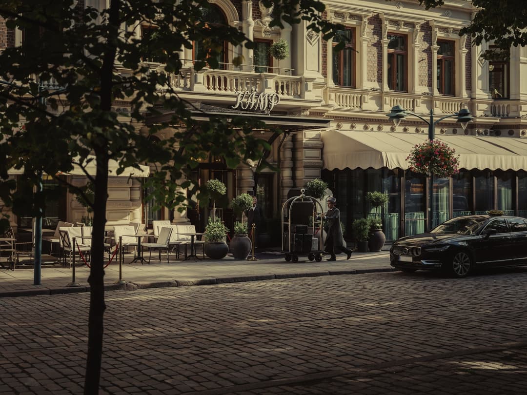 Facade of Hotel Kämp with cafe terrace, luggage trolley and a parked car
