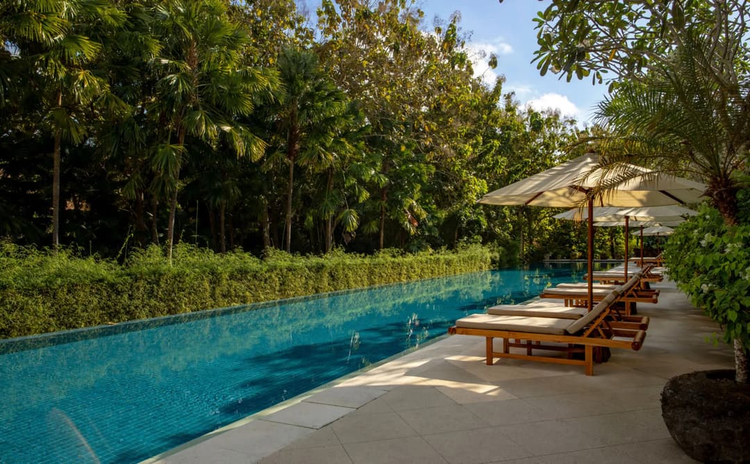 Resort swimming pool at Aman Villas at Nusa Dua, flanked by loungers and tropical trees