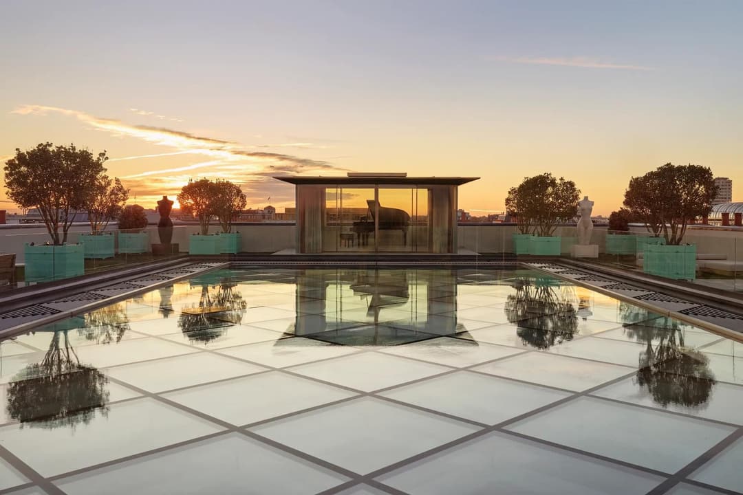 Glass-roof terrace at Claridge’s with a pavilion housing a grand piano, surrounded by trees and sculptures at sunset, Claridge's