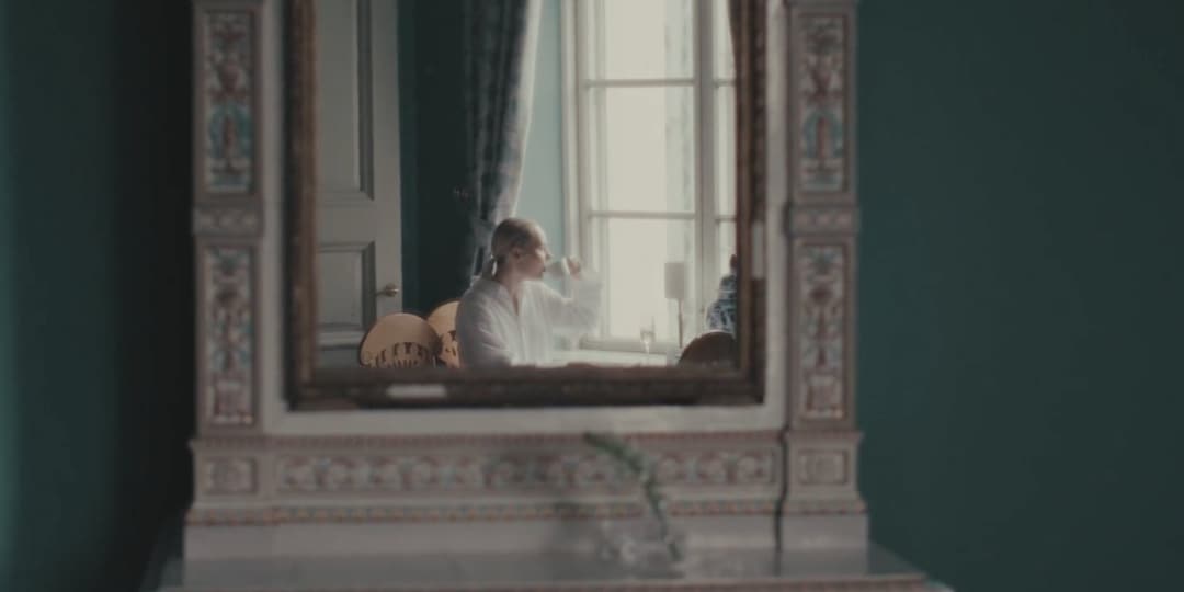 Ornate gilt mirror on a green wall reflecting a guest by a window at Hotel Haven