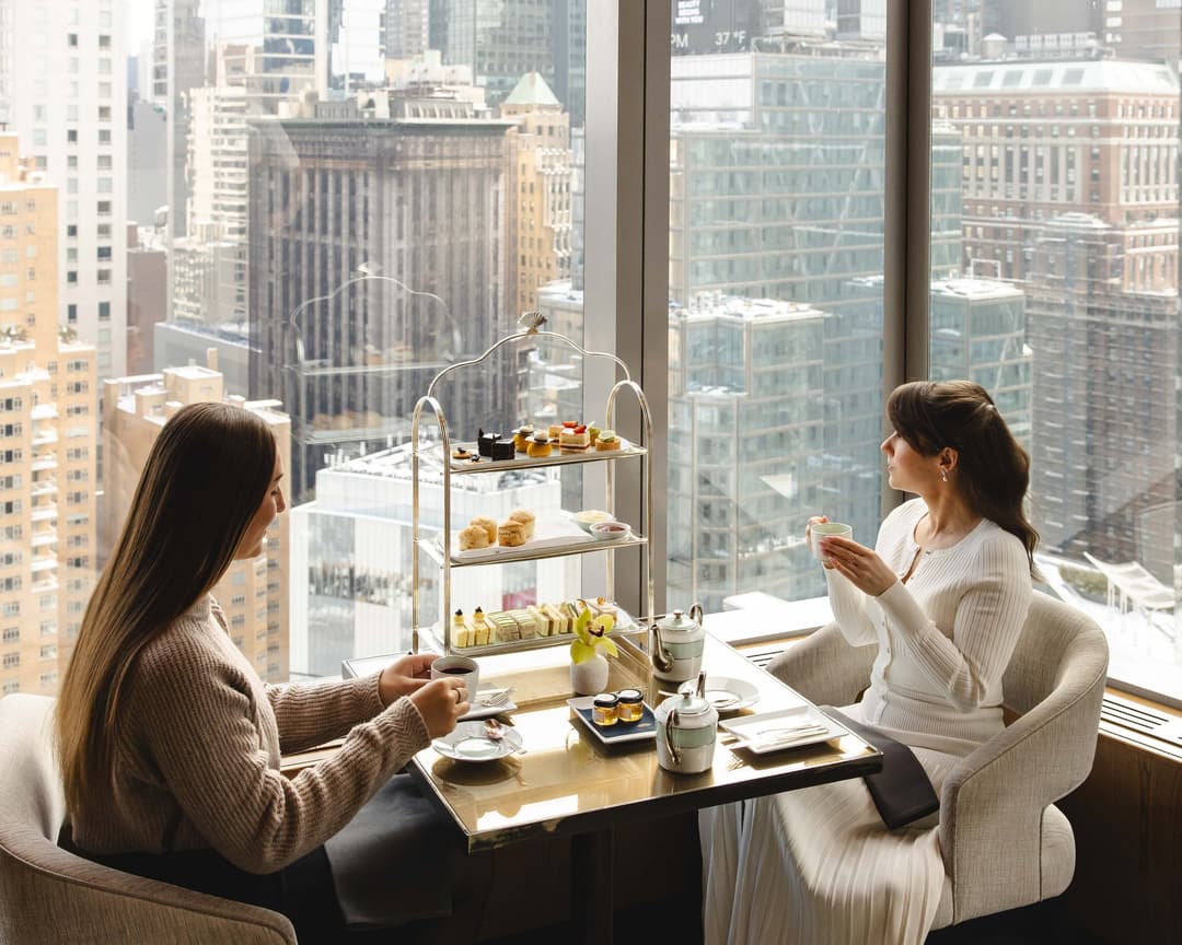 Two guests taking afternoon tea by floor-to-ceiling windows at Mandarin Oriental, New York