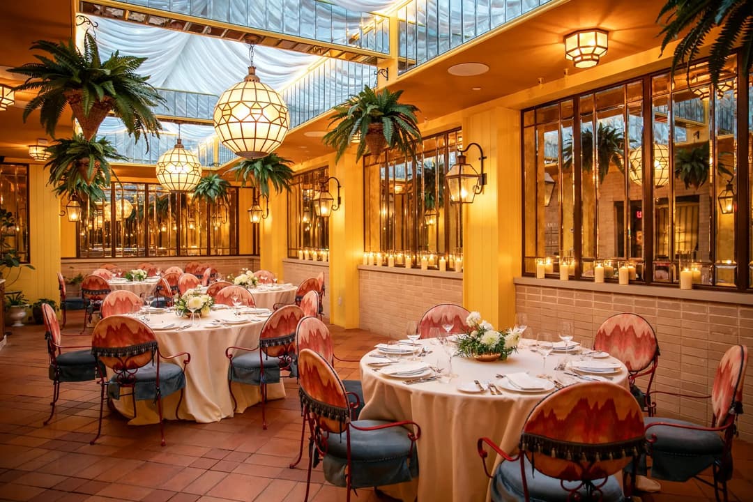 Glass-roofed dining room with ferns, pendant lanterns and round tables at The Fifth Avenue Hotel