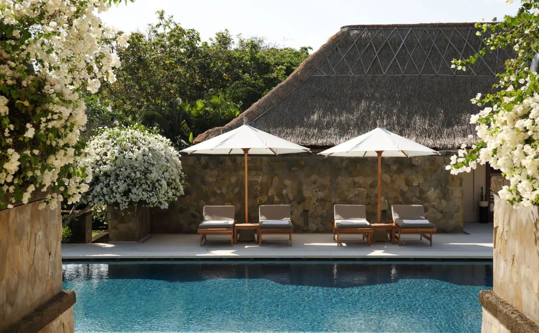 Resort swimming pool at Aman Villas at Nusa Dua, Indonesia, with thatched pavilion and loungers