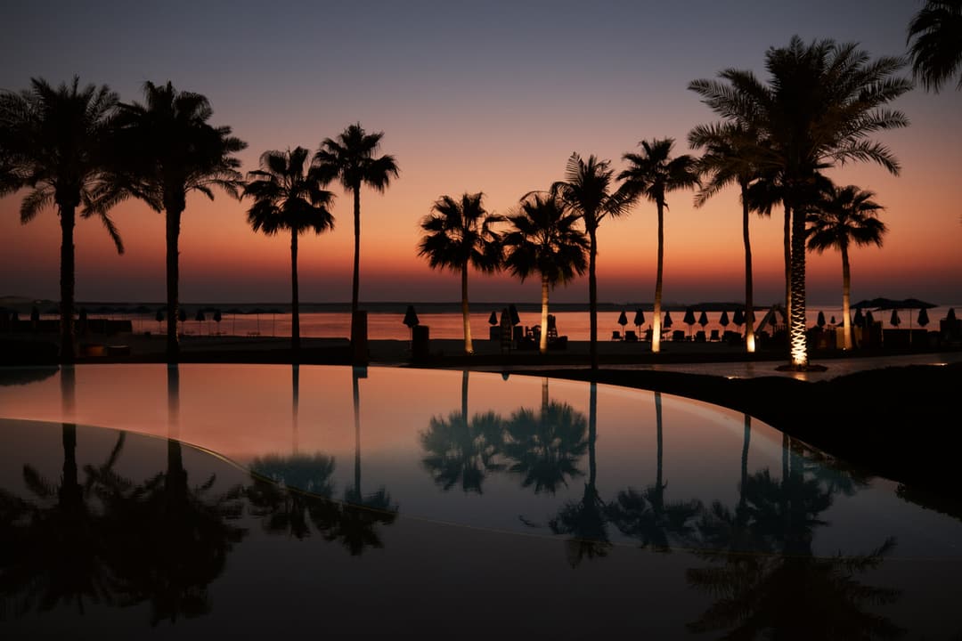 A palm tree?lined pool with the beach in the background all lit under a dark orange and blue sky as the sun sets, Four Seasons Resort Dubai at Jumeira