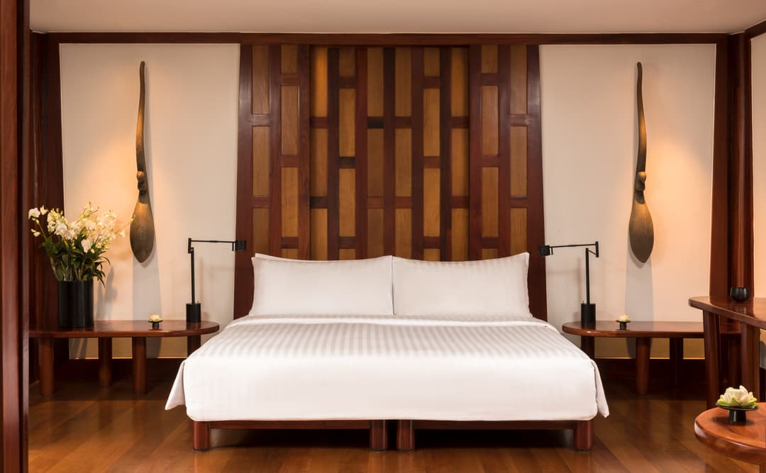 Amanpuri bedroom pavilion with wooden feature wall, pendant lights and white bed, Phuket