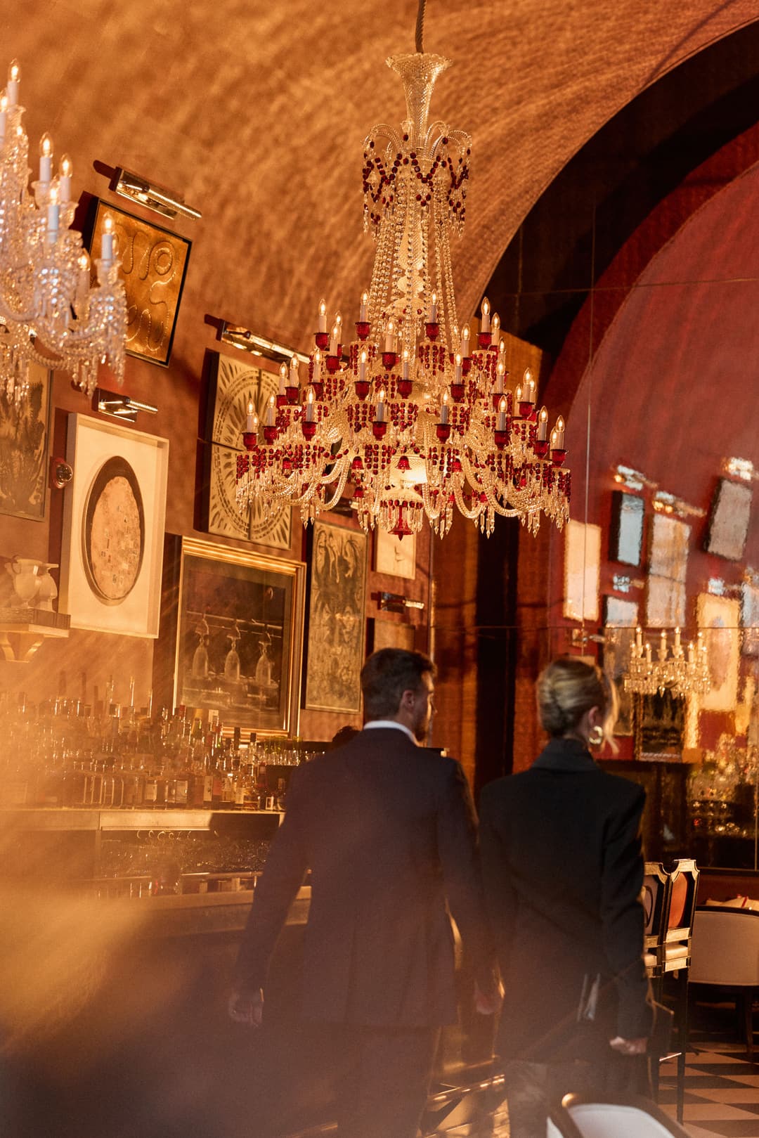 Man and women walking hand in hand under an ornate chandelier in a bar