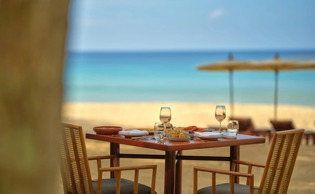 Amanpuri dining table setup overlooking Thailand's coastline, with wooden chairs and beachfront views