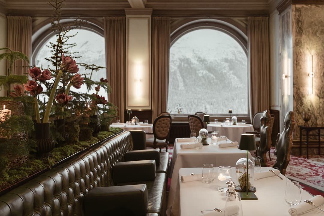 Fine dining restaurant with tall arched windows, festive round tables, and luxurious leather furniture, Carlton Hotel St. Moritz