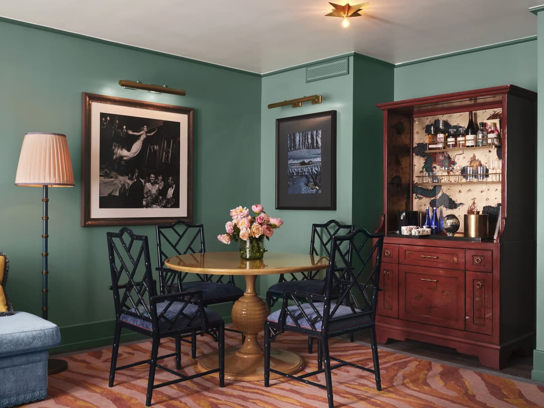 Teal dining nook with a round table, framed photos and a red bar cabinet at The Fifth Avenue Hotel