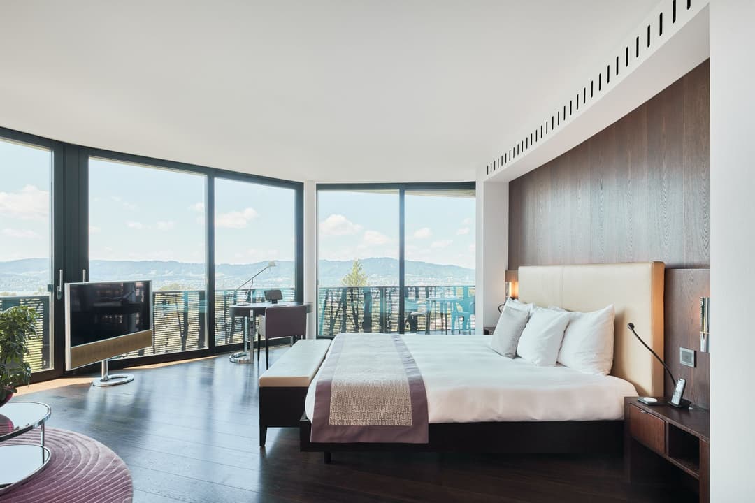 Ein modernes Zimmer im Dolder Grand mit großem Bett, Holzböden, raumhohen Fenstern und Schreibtisch