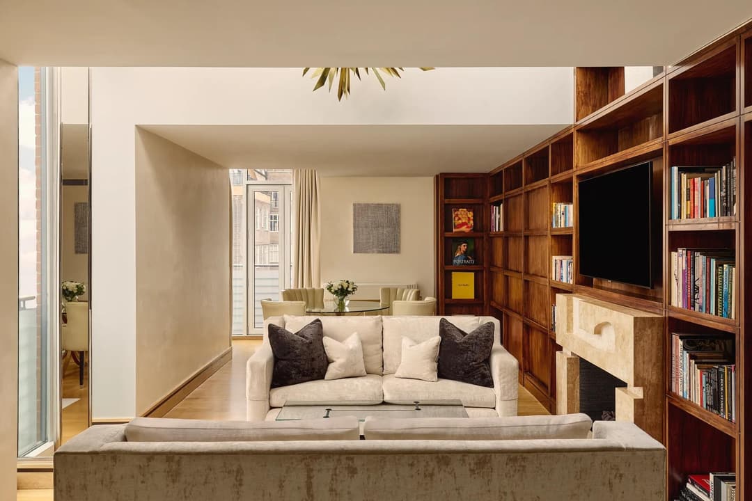 Spacious suite with cream sofas, wood bookcase wall, fireplace and dining table near balcony, The Connaught
