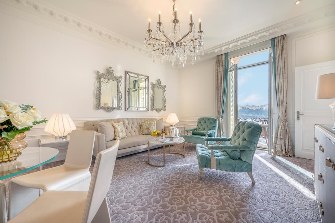 Living room with teal armchairs, a crystal chandelier and balcony doors at Hotel Hermitage Monte Carlo