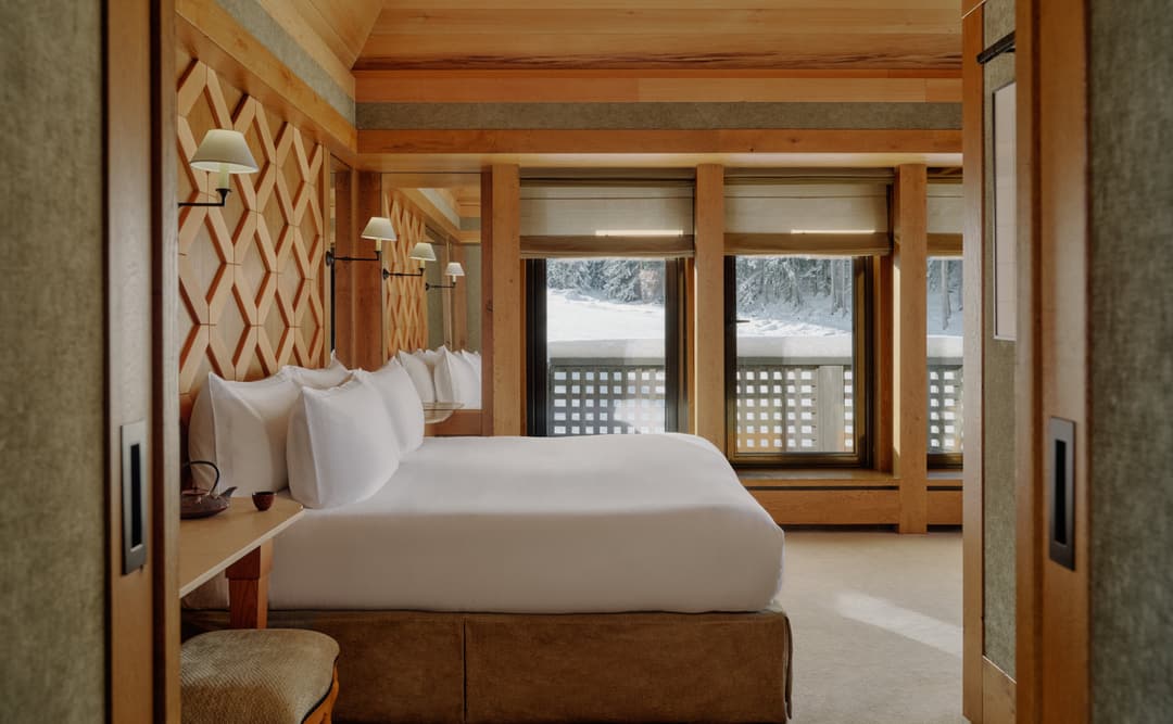Vanoise Suite bedroom at Aman Le Mélézin with wooden bed frame and alpine views through large windows.