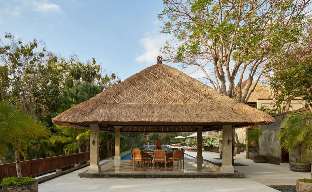 Dining bale with thatched roof at Aman Villas at Nusa Dua, Indonesia, surrounded by tropical greenery