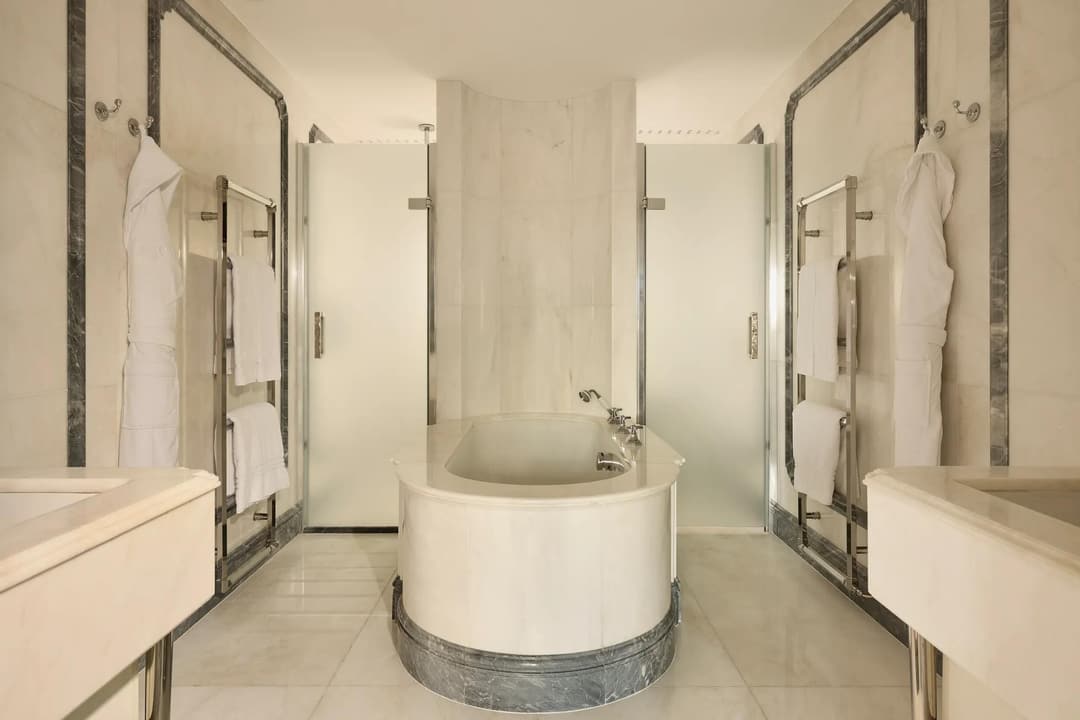 Luxurious marble bathroom with central oval bathtub, frosted glass doors, and towel rails, The Connaught