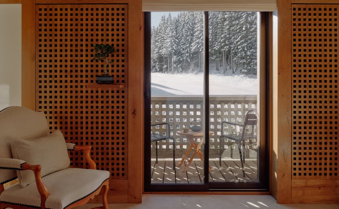 Bedroom at Aman Le Mélézin with glazed doors opening onto a snow-covered balcony and alpine views.