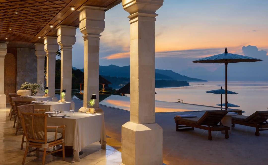 Amankila's clifftop dining venue at sunset, with stone columns framing views across Bali's coastline