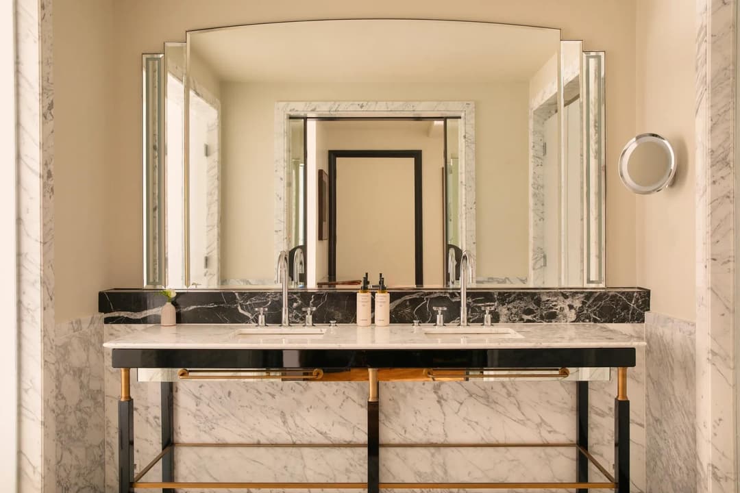 Double marble vanity with illuminated mirrors, twin basins and brass accents in a spacious bathroom, Claridge's