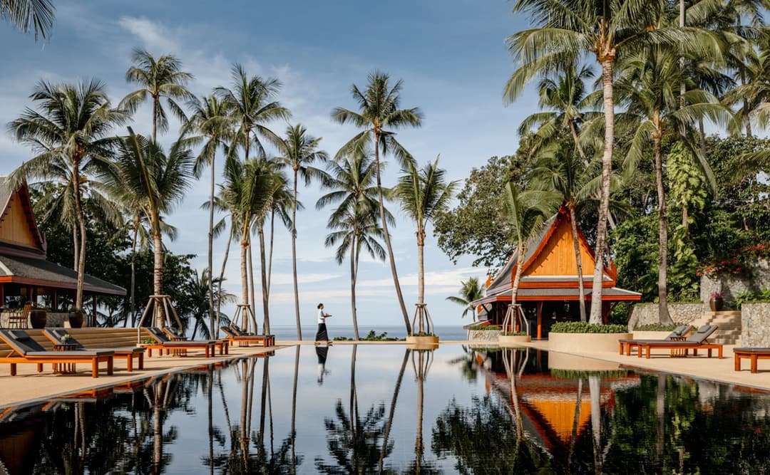 Amanpuri's wooden pavilions reflect in still water surrounded by palm trees at dawn, Aman Nai Lert Bangkok