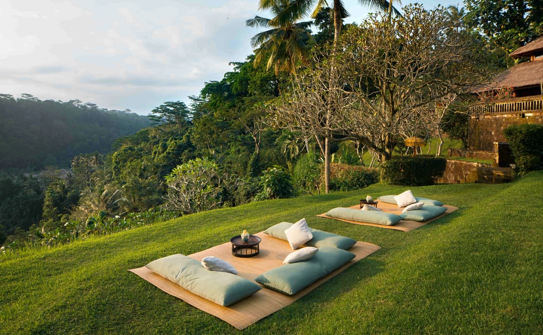Sundowner picnic setup on a manicured lawn at Amandari, with cushioned seating arranged on the grass overlooking verdant valley views