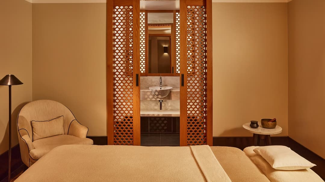 Tranquil spa room with a treatment bed, soft armchair, and carved wooden screens revealing a small sink area, The Connaught