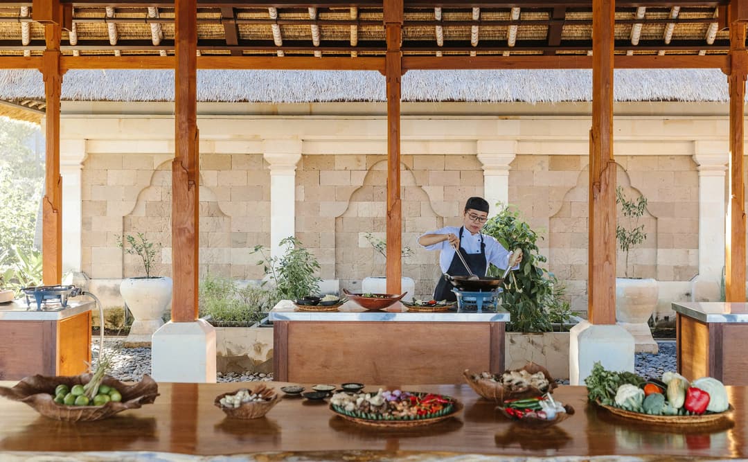 Chef instructing guests during a cooking class at Amankila, with open-sided pavilion overlooking tropical gardens