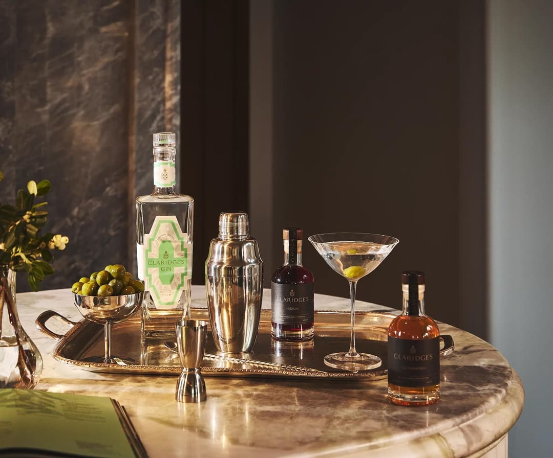 Marble table with cocktail setup, including martini glass, shaker, spirits, olives, and Claridge’s gin bottle, Claridge's