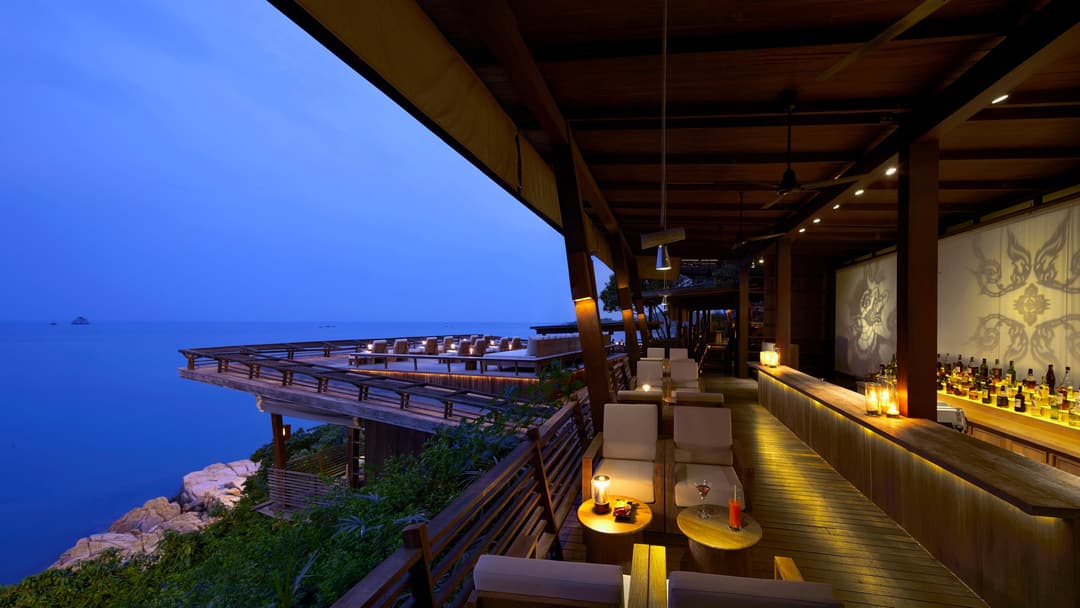 Restaurant and bar with contemporary seating and gentle lighting; tables offer views of the ocean and rocky shoreline in the evening, Six Senses Samui