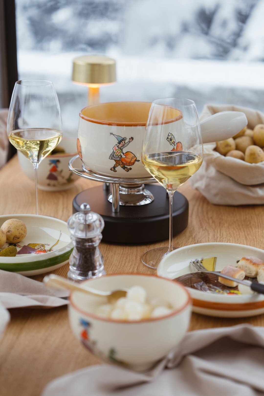 Elegant table setting with white wine glasses, decorative fondue pot with illustrated design, and appetizer plates on wood table, Carlton Hotel St. Mo