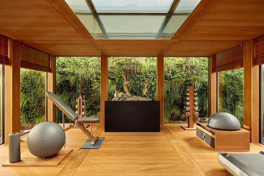 Private fitness room at Claridge’s with wood interiors, gym equipment, and floor-to-ceiling windows overlooking a green wall, Claridge's